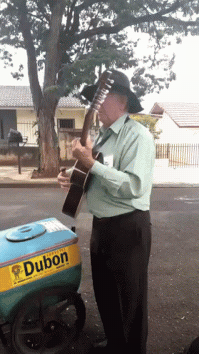 A Man Playing A Guitar In Front Of A Dubon Ice Cream Cart GIF