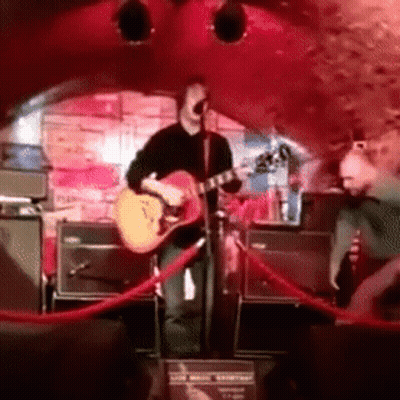 A Man Playing A Guitar In Front Of A Microphone GIF