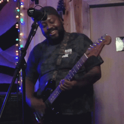 A Man Playing A Guitar In Front Of A Microphone With A Sign On The Wall That Says No Smoking GIF