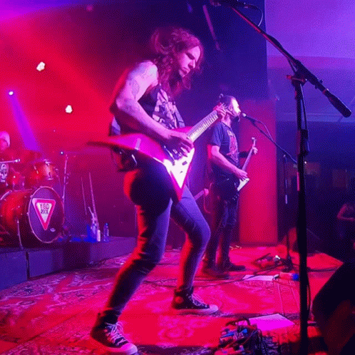 A Man Playing A Guitar In Front Of A Microphone With A Triangle On The Drum Set GIF