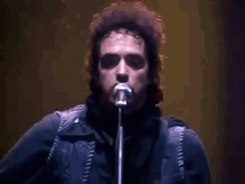 A Man Playing A Guitar On A Stage In Front Of A Band GIF