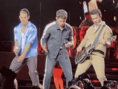 A Man Playing A Guitar On Stage With Two Other Men GIF