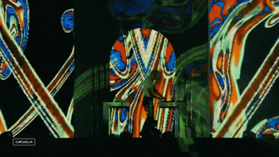 A Man Playing A Keyboard In Front Of A Colorful Screen That Says Gazelle GIF