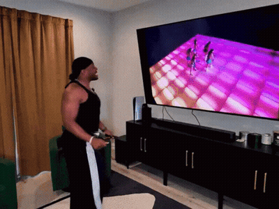A Man Playing A Video Game In Front Of A Large Flat Screen Tv GIF