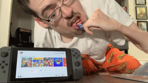 A Man Playing A Video Game On A Nintendo Switch While Wearing Reeses Pajamas GIF