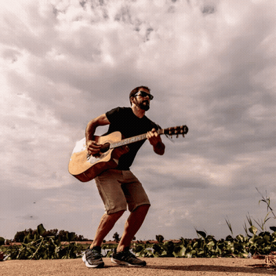 A Man Playing An Acoustic Guitar On A Dirt Road GIF