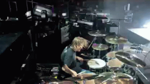 A Man Playing Drums In A Dark Room With A Drum Set GIF