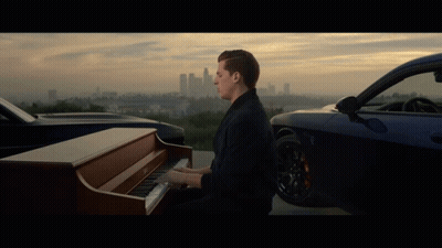 A Man Plays A Piano In Front Of A Car GIF