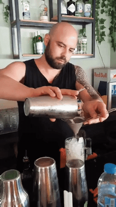 A Man Pouring A Drink In Front Of A Red Bull Cooler GIF