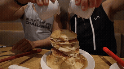 A Man Pouring Syrup On A Stack Of Pancakes With A Shirt That Says Built For Challenges GIF