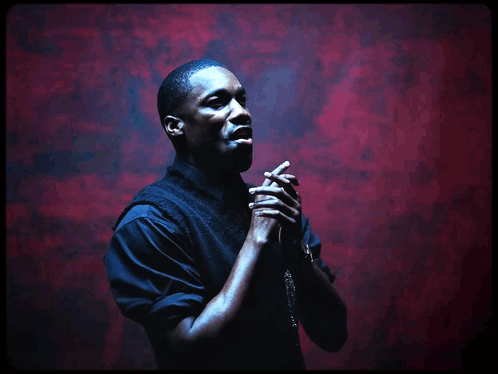 A Man Praying With His Hands Folded In Front Of A Red Background GIF