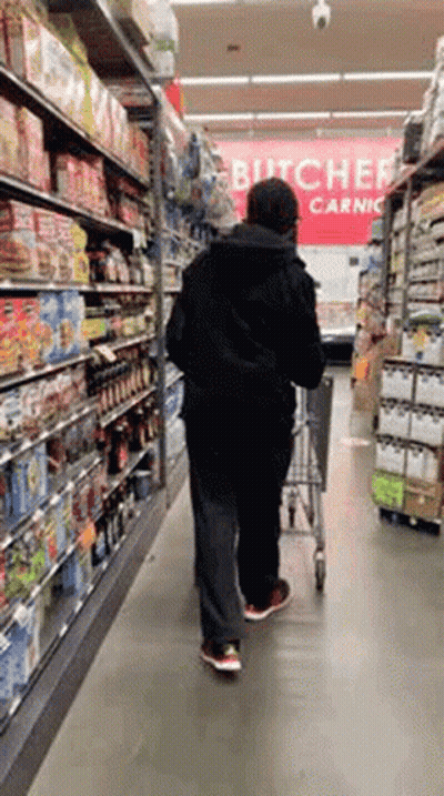 A Man Pushing A Shopping Cart In A Grocery Store With A Sign That Says Butcher Carnic GIF