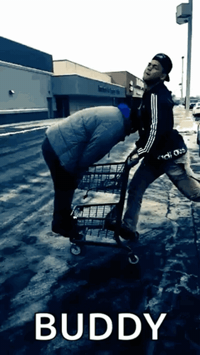 A Man Pushing Another Man In A Shopping Cart With The Word Buddy Below Him GIF