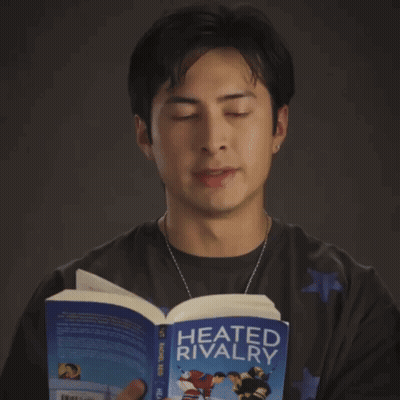A Man Reads A Book Called Heated Rivalry GIF