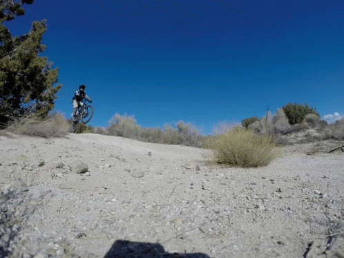 A Man Riding A Bike Down A Dirt Road GIF