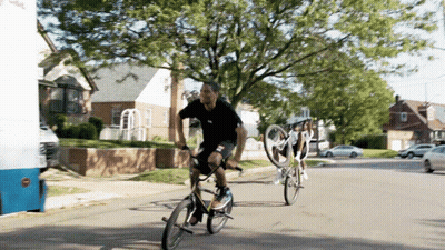 A Man Riding A Bike On A Street Next To A White Van That Says ' Ice Cream ' On It GIF