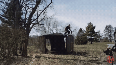 A Man Riding A Bike On Top Of A Wooden Structure In A Field GIF