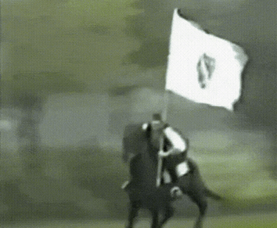 A Man Riding A Horse Holding A White Flag With The Letter S On It GIF