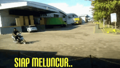 A Man Riding A Motorcycle In Front Of A Warehouse With The Words Siap Meluncur Written On The Bottom GIF