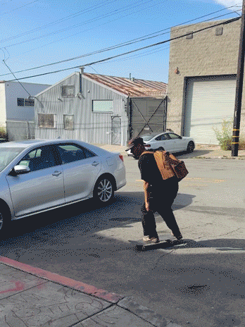 A Man Riding A Skateboard Down A Street With A Bag On His Back GIF