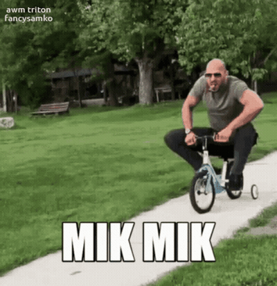 A Man Riding A Tricycle On A Sidewalk With Mik Mik Written On The Side GIF