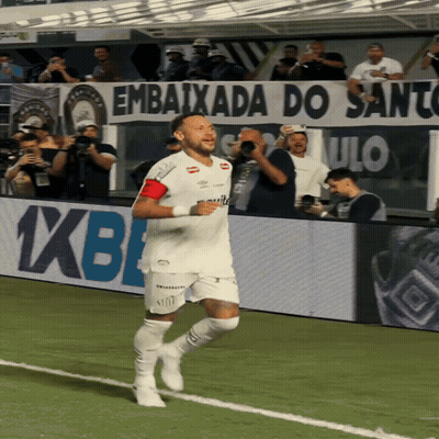 A Man Running On A Soccer Field With A Banner Behind Him That Says " Embaixada Do Santos " GIF