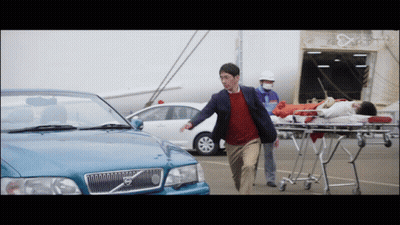 A Man Running Towards A Volvo Car With A Woman On A Stretcher Behind Him GIF
