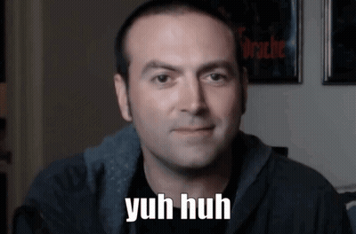 A Man Says Yuh Huh In Front Of A Wall With Pictures On It GIF