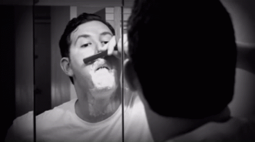 A Man Shaves In Front Of A Mirror With A Razor GIF