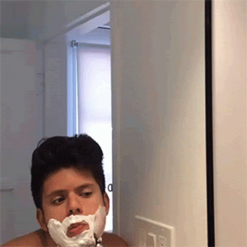 A Man Shaving His Face In Front Of A Mirror With Foam On His Face GIF