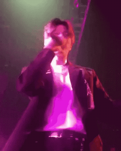 A Man Singing Into A Microphone In A Purple Light GIF