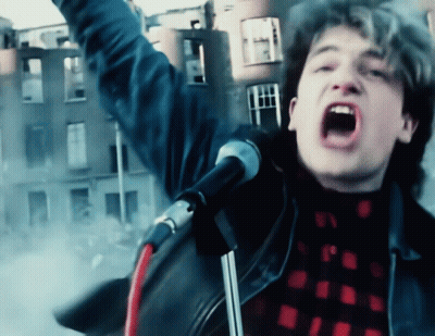 A Man Singing Into A Microphone In Front Of A Building GIF