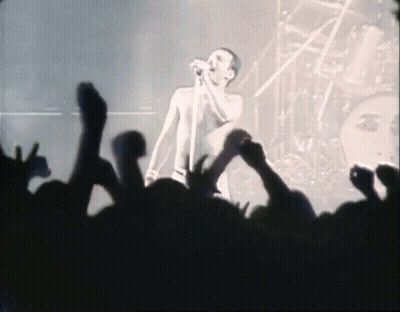 A Man Singing Into A Microphone In Front Of A Crowd Of People GIF