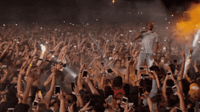 A Man Singing Into A Microphone In Front Of A Crowd Of People Holding Up Their Phones GIF