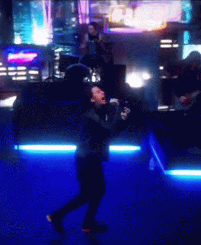 A Man Singing Into A Microphone In Front Of A Crowd GIF