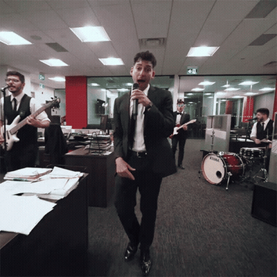 A Man Singing Into A Microphone In Front Of A Drum Set That Says Tama GIF
