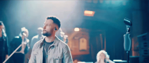 A Man Singing Into A Microphone In Front Of A Group Of People GIF
