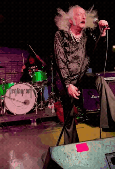 A Man Singing Into A Microphone In Front Of A Pentagram Drum GIF