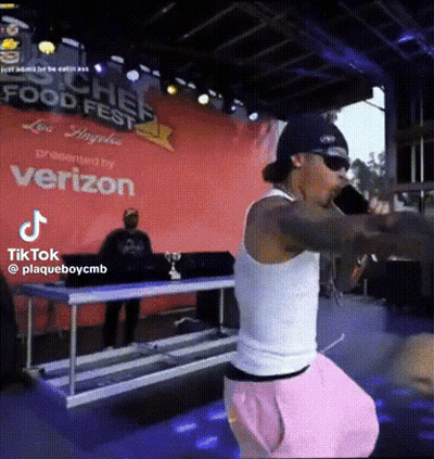 A Man Singing Into A Microphone In Front Of A Sign That Says Food Fest GIF