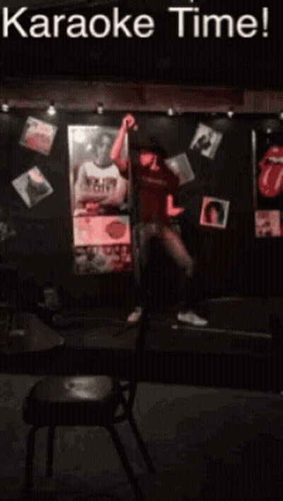 A Man Singing Into A Microphone In Front Of A Sign That Says Karaoke Time ! GIF