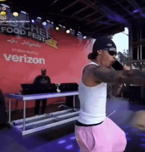 A Man Singing Into A Microphone In Front Of A Verizon Banner GIF