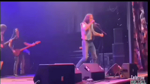 A Man Singing Into A Microphone On A Stage With Carlos Live Written On The Bottom Right GIF