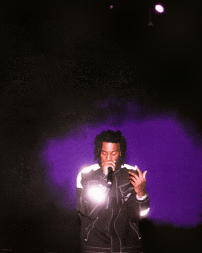 A Man Singing Into A Microphone Wearing A Jacket That Says ' Dg ' On It GIF