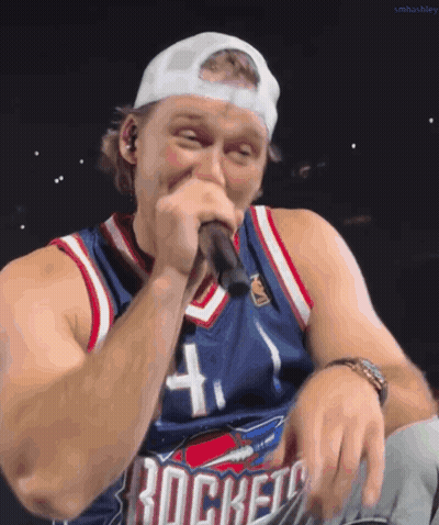 A Man Singing Into A Microphone Wearing A Rockets Jersey GIF