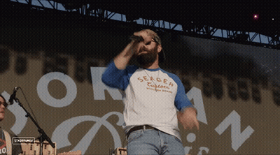 A Man Singing Into A Microphone Wearing A Shirt That Says Serger Customs GIF