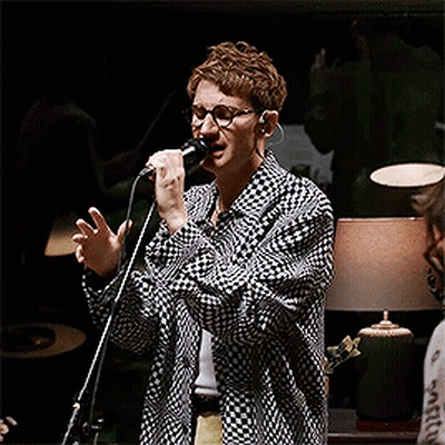A Man Singing Into A Microphone Wearing Glasses And A Plaid Shirt GIF