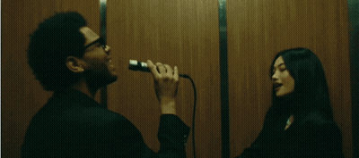 A Man Singing Into A Microphone While A Woman Looks On GIF