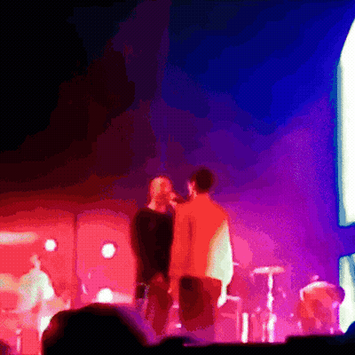 A Man Singing Into A Microphone While Another Man Looks On GIF
