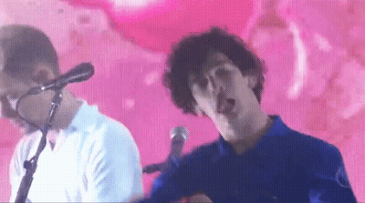 A Man Singing Into A Microphone While Another Man Looks On GIF