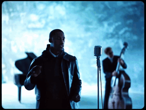 A Man Singing Into A Microphone While Another Man Plays A Bass GIF